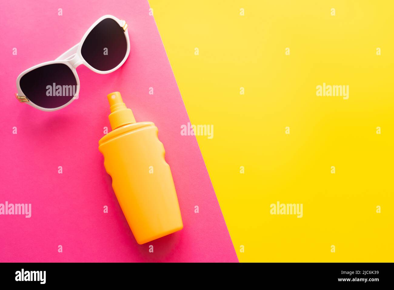 Top view of sunglasses and sunblock on pink and yellow background Stock Photo
