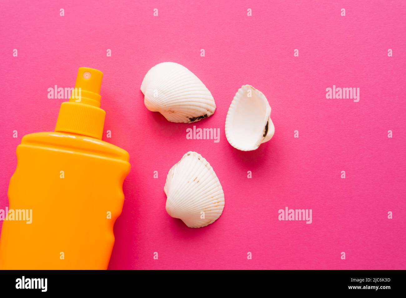 Top view of seashells and bottle of sunscreen on pink surface Stock Photo