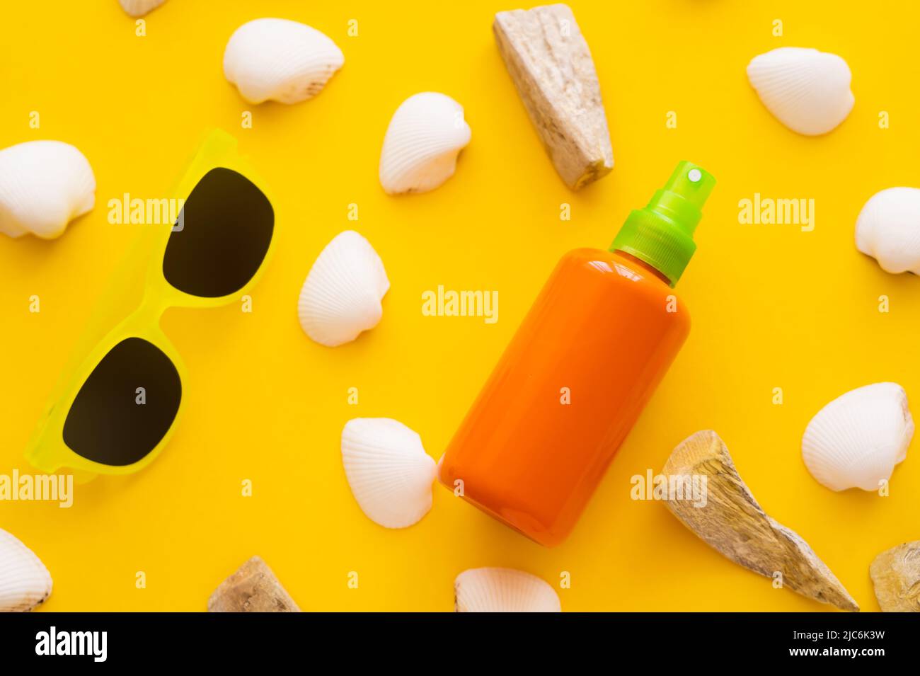 Top view of sunblock near seashells and sunglasses on yellow background Stock Photo