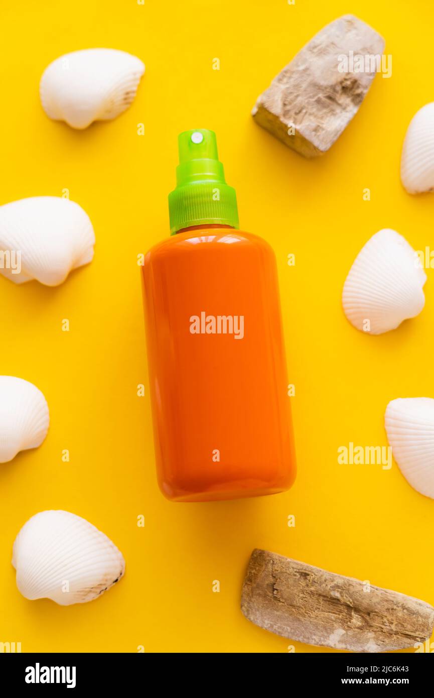 Top view of bottle of sunscreen near seashells and stones on yellow background Stock Photo