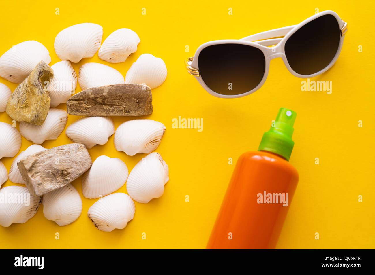 Top view of sunglasses near seashells and sunblock on yellow background Stock Photo