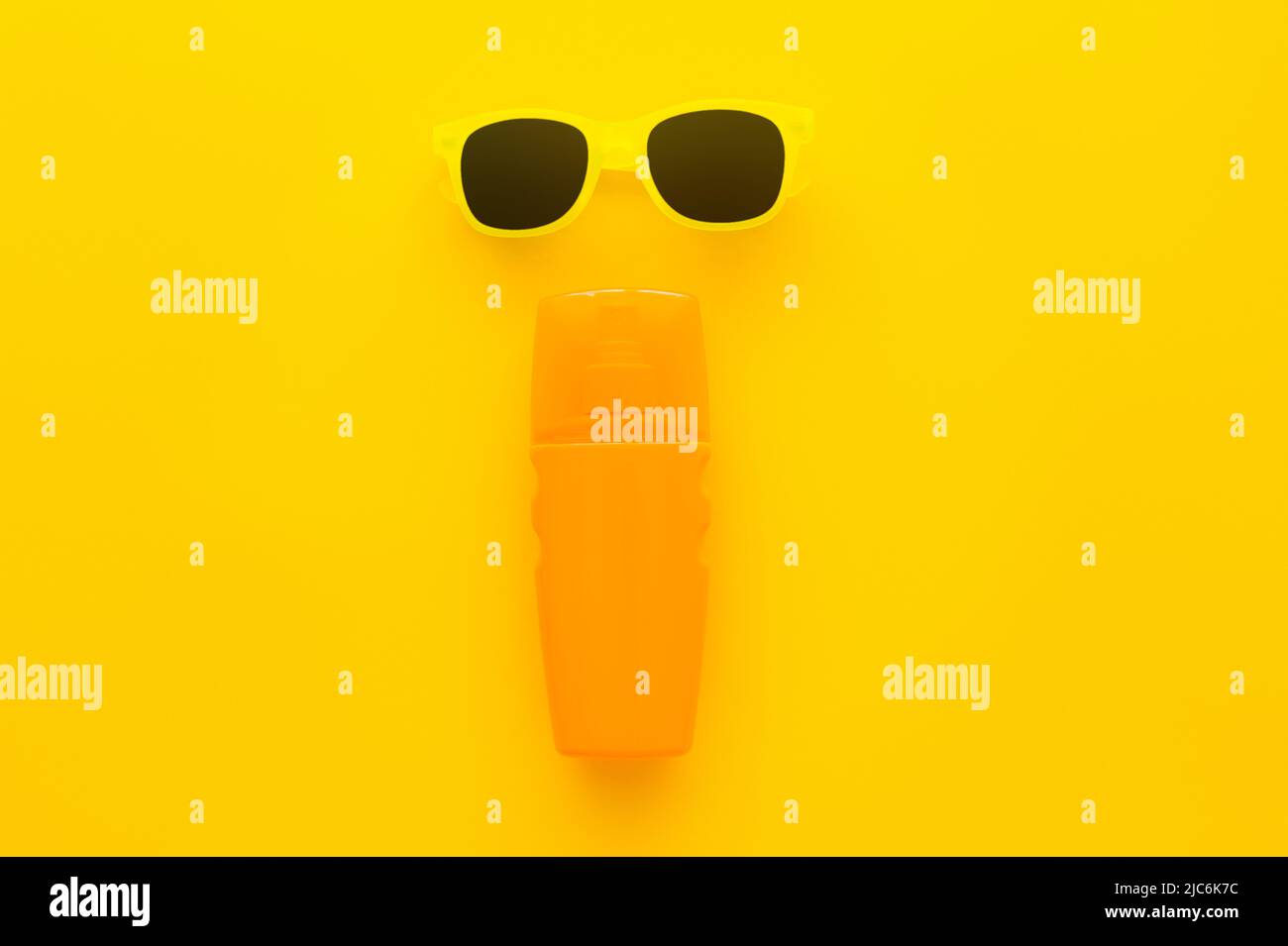 Top view of sunglasses and bottle of sunscreen on yellow background Stock Photo