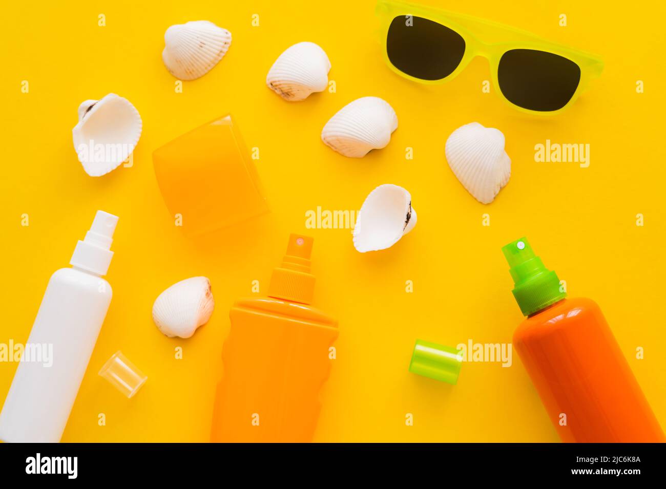 Top view of seashells near sunscreens and sunglasses on yellow background Stock Photo