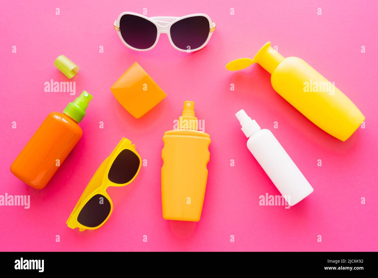 Top view of sunscreens with caps and sunglasses on pink surface Stock Photo