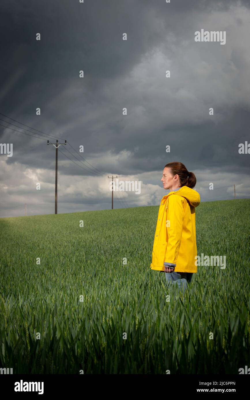 Portrait of a woman wearing a yellow coat in a green field with a stormy sky background. Stock Photo