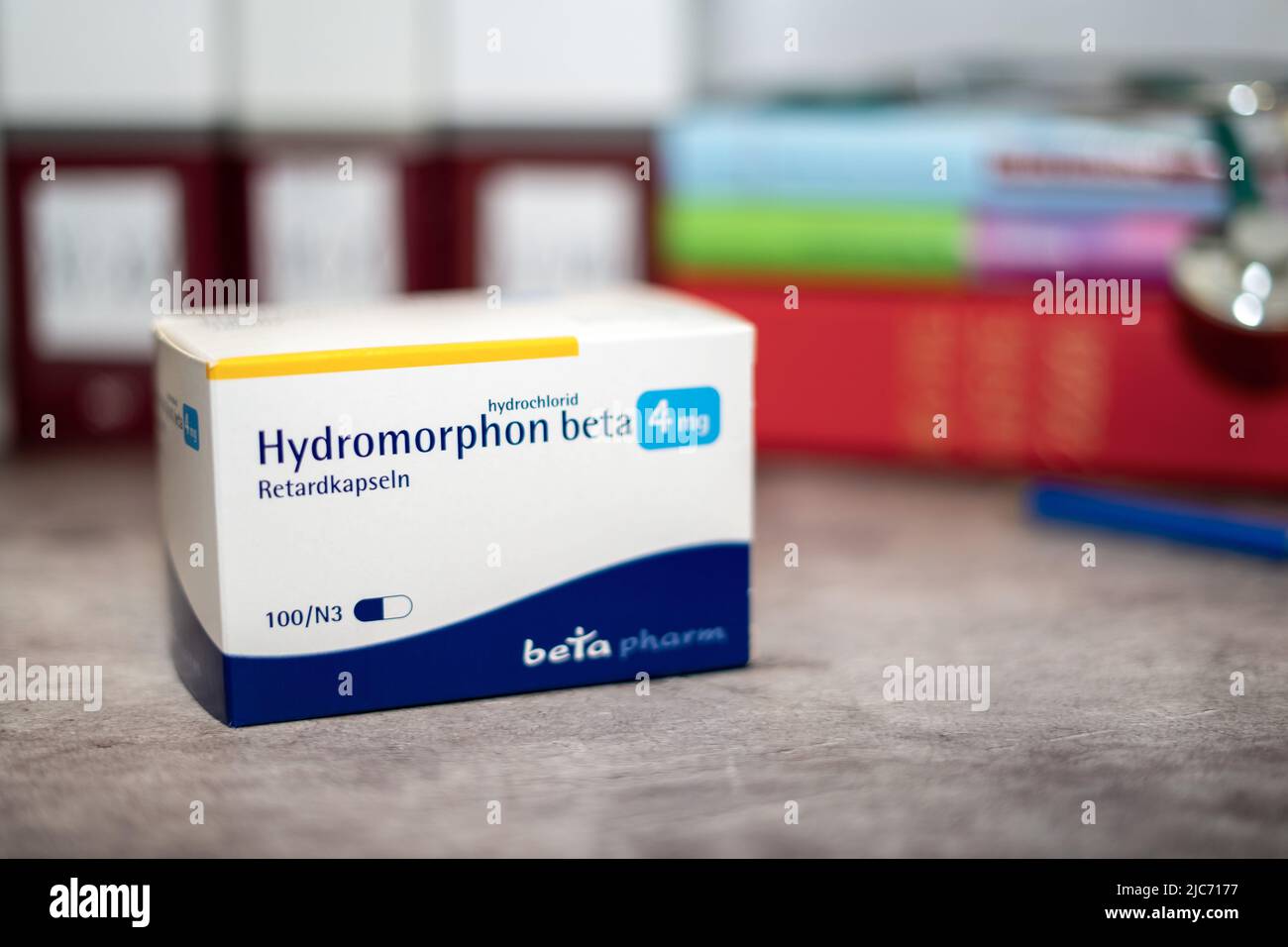 Hydromorphon drug box containing Hydromorphon recommended for pain due to cancer, on a table and in the background different medical books. Stock Photo