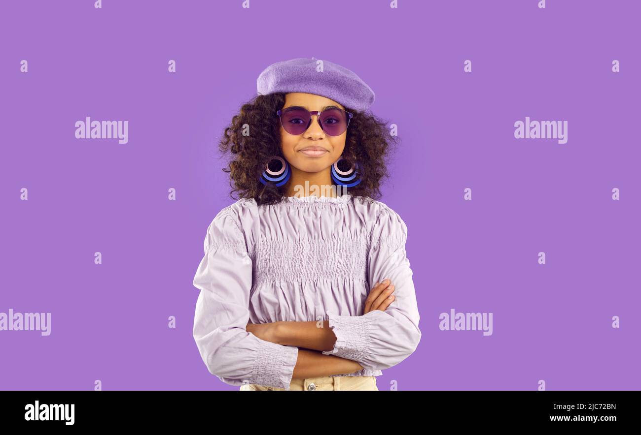 Happy beautiful child in trendy top, beret hat and sunglasses standing on purple background Stock Photo