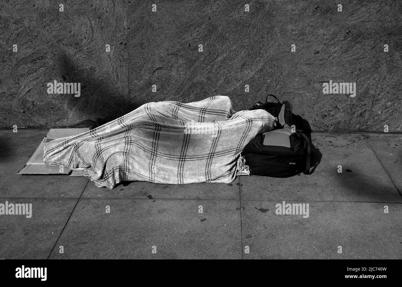 A homeless man sleeps under a blanket on a sidewalk in San Francisco