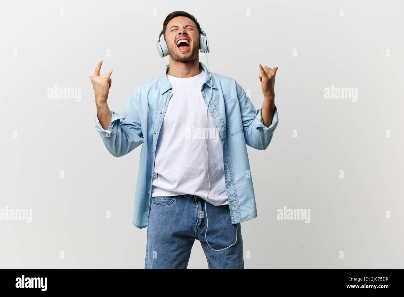 Crazy overjoyed handsome man in casual basic tshirt headphones show horns up gesture, heavy