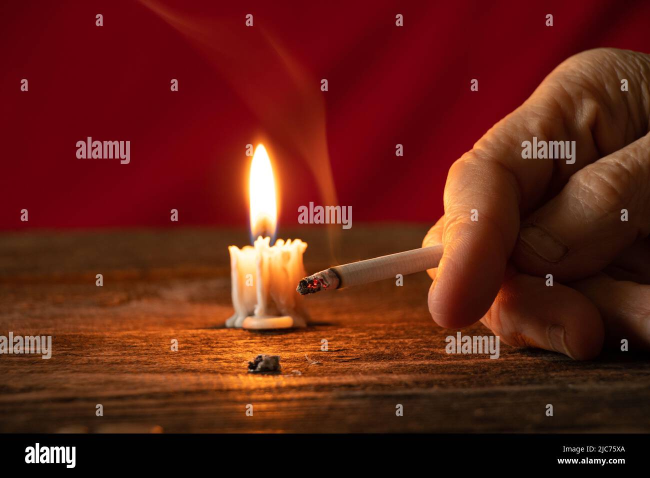 old woman holding a cigarette by candlelight in the dark at home at the  table, smoking at home in the dark, nicotine and bad habit, cigarettes and  can Stock Photo