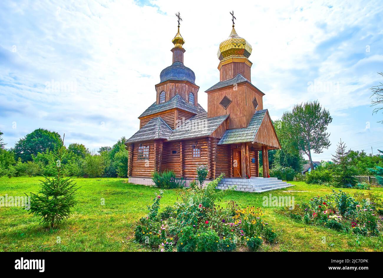 The scenic wooden Church of the Intercession with golden domes and its garden in Cherevki village, Ukraine Stock Photo