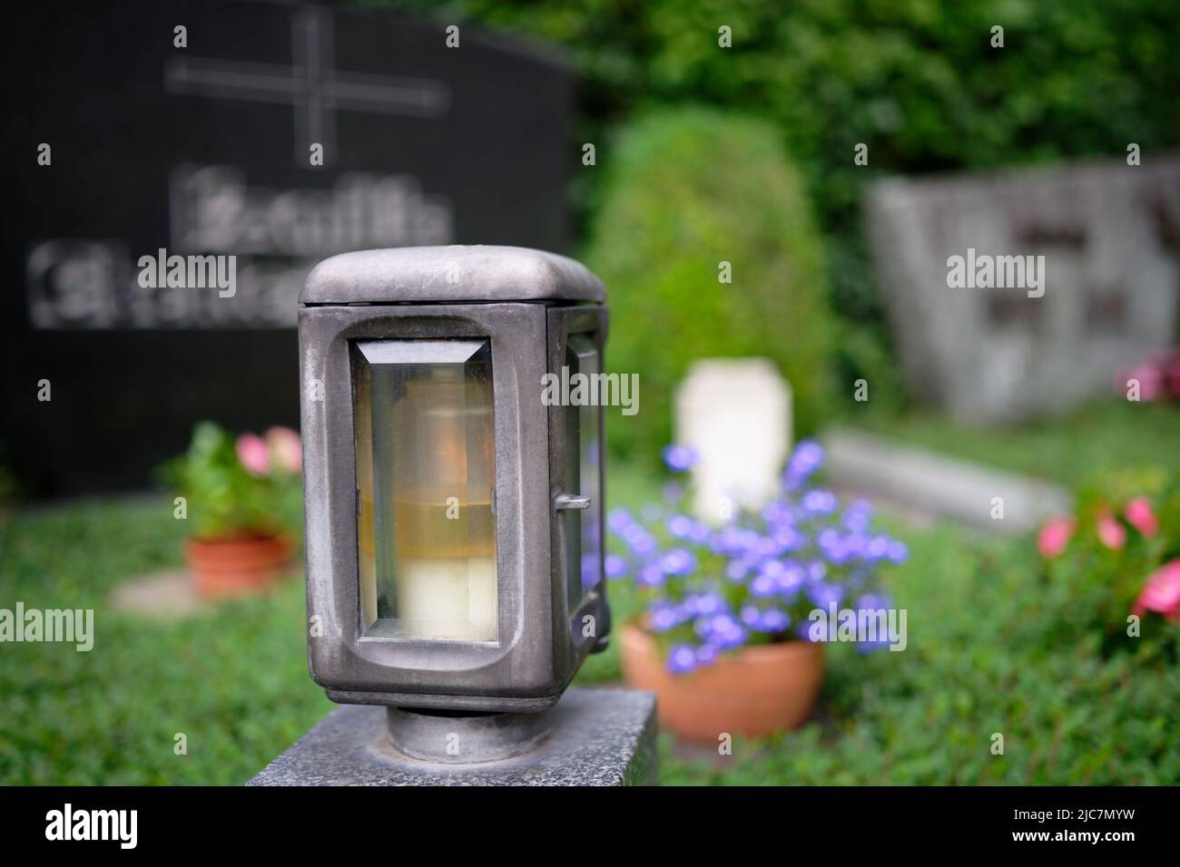 grave lantern with flowers and tombstone in blurred background Stock Photo