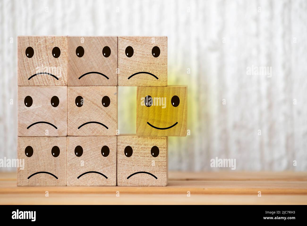 wooden cubes with smiling emoticons and sad one on wood table, blue background. Space for text. emotional state concept Stock Photo