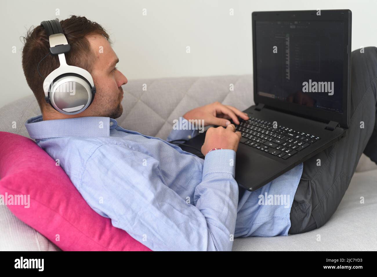 Young man freelancer working from home with his laptop laying on couch Stock Photo
