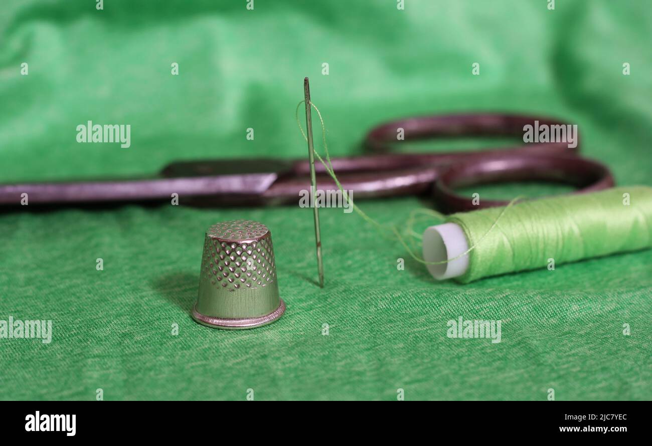 Spool of Green Thread, Thimble and Needle on Green Fabric Stock Photo