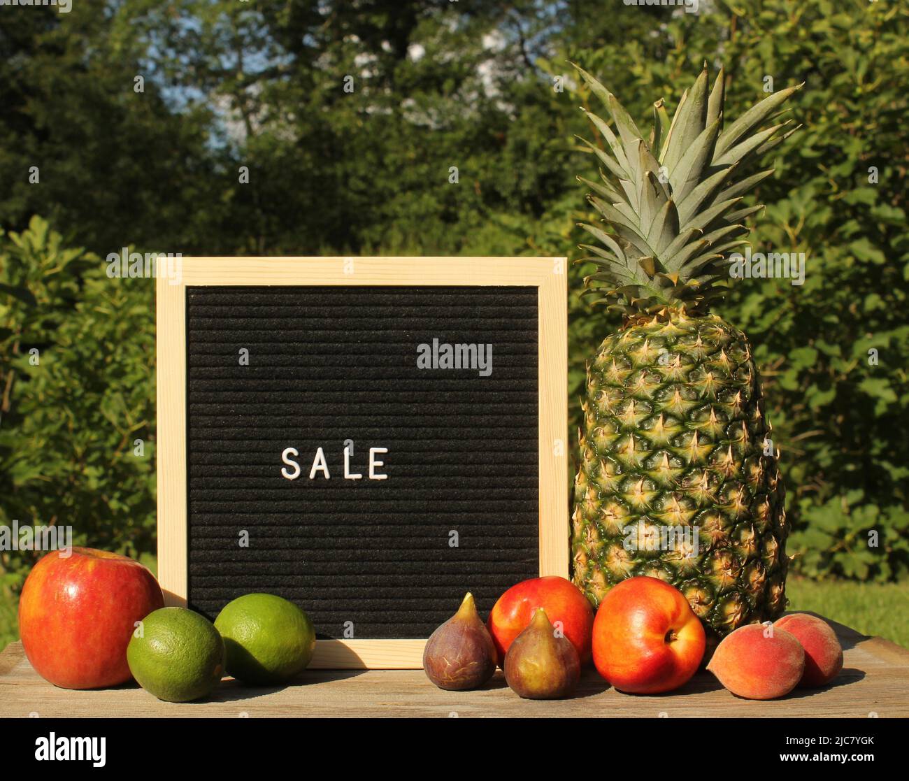 Fresh Pineapple outdoors with Apricots, Peaches and figs. sale sign garden in background Stock Photo