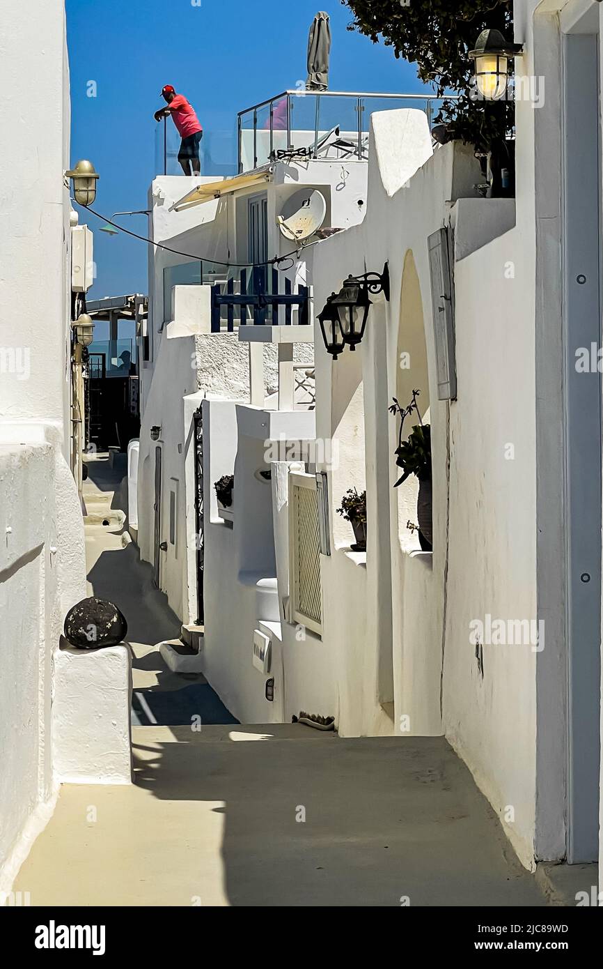 A man leans over the railing on a roof terrace above a narrow lane in Imerovigli on Santorini island Stock Photo