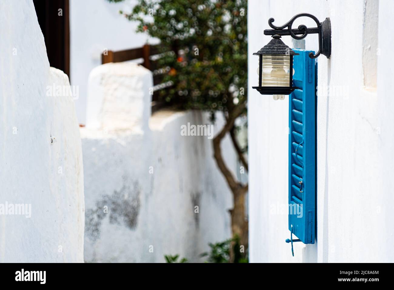 Santorini: A side alley in the town of Megalochori with a traditional sky blue shutter and a lantern on a whitewashed wall Stock Photo