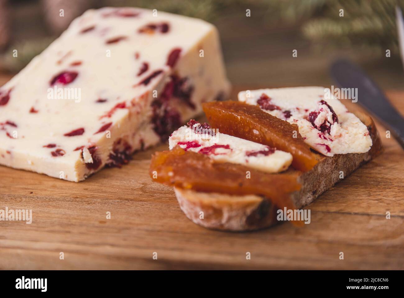 Wensleydale cheese with cranberries, red wine, honey, nuts, raisins on marble cutting board. Black concrete background. Selective focus. Stock Photo