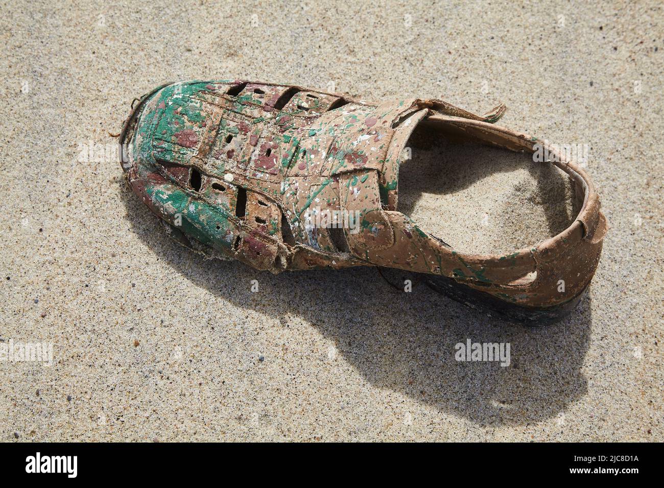 Old torn sandal spattered with paint on the sandy shore. Loneliness and ...
