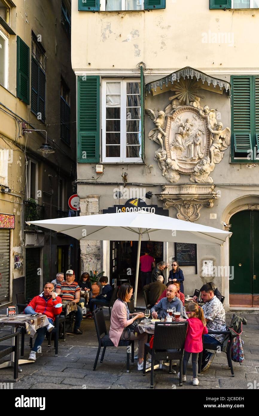 People sitting at a sidewalk cafè under a majestic votive shrine in Piazza Pollaiuoli, in the old town of Genoa, Liguria, Italy Stock Photo