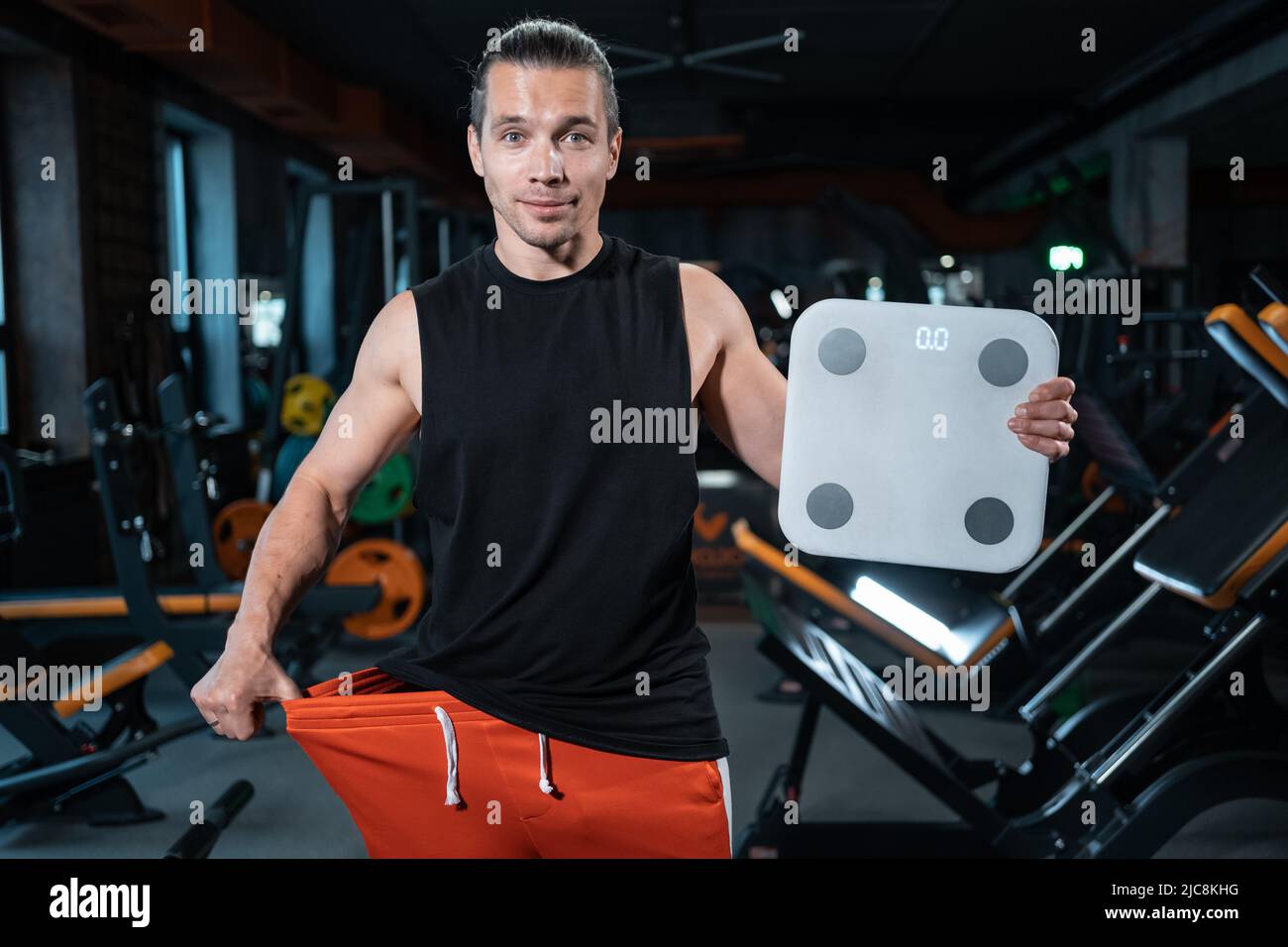 young attractive athlete male weight with scale in gym and dieting Stock Photo