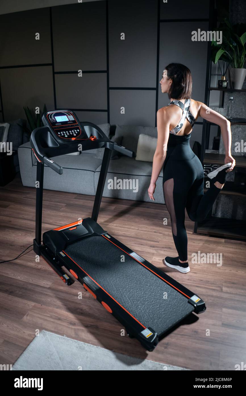 cheerful female stretching and preparing for cardio workout on treadmill at home Stock Photo