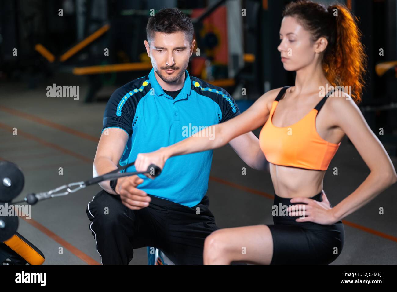 young woman exercising single arm row kneeling with personal trainer man in gym Stock Photo