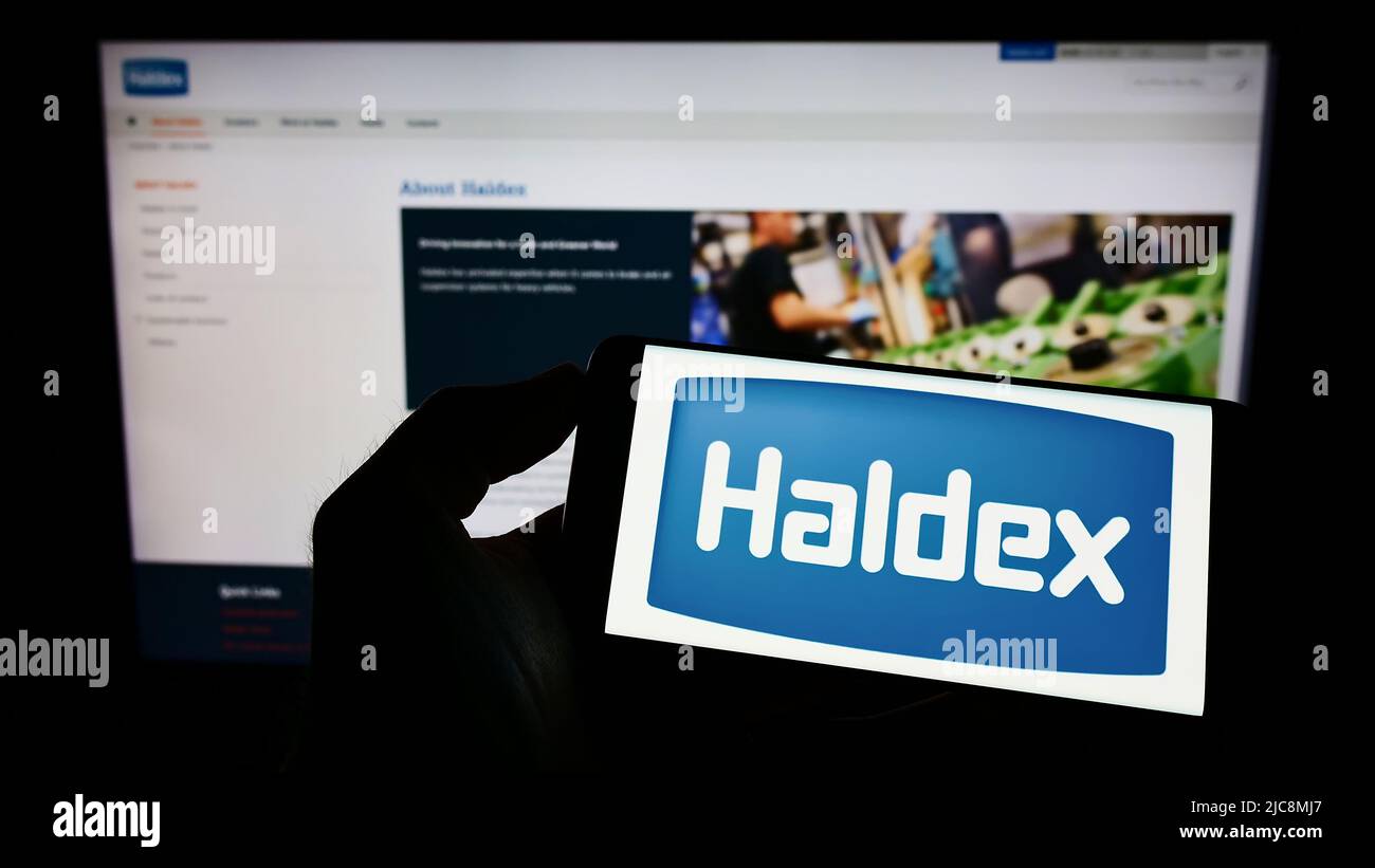 Person holding smartphone with logo of automotive company Haldex Europe SAS on screen in front of website. Focus on phone display. Stock Photo