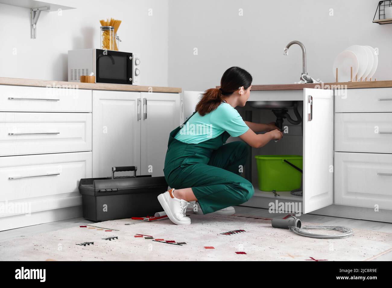 Female plumber fixing sink in kitchen Stock Photo