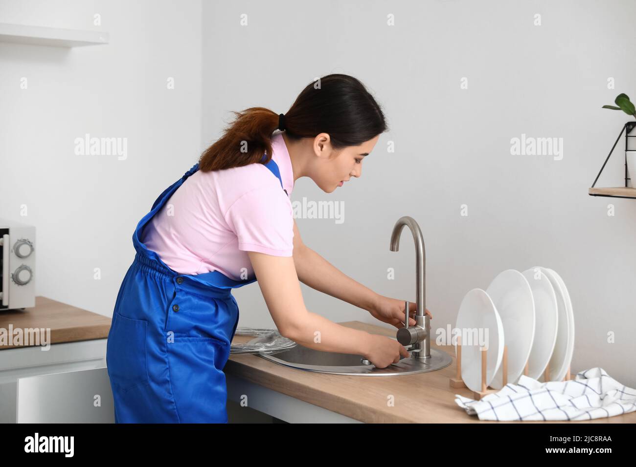 A female plumber fixing the kitchen sink with a plunger, Stock image