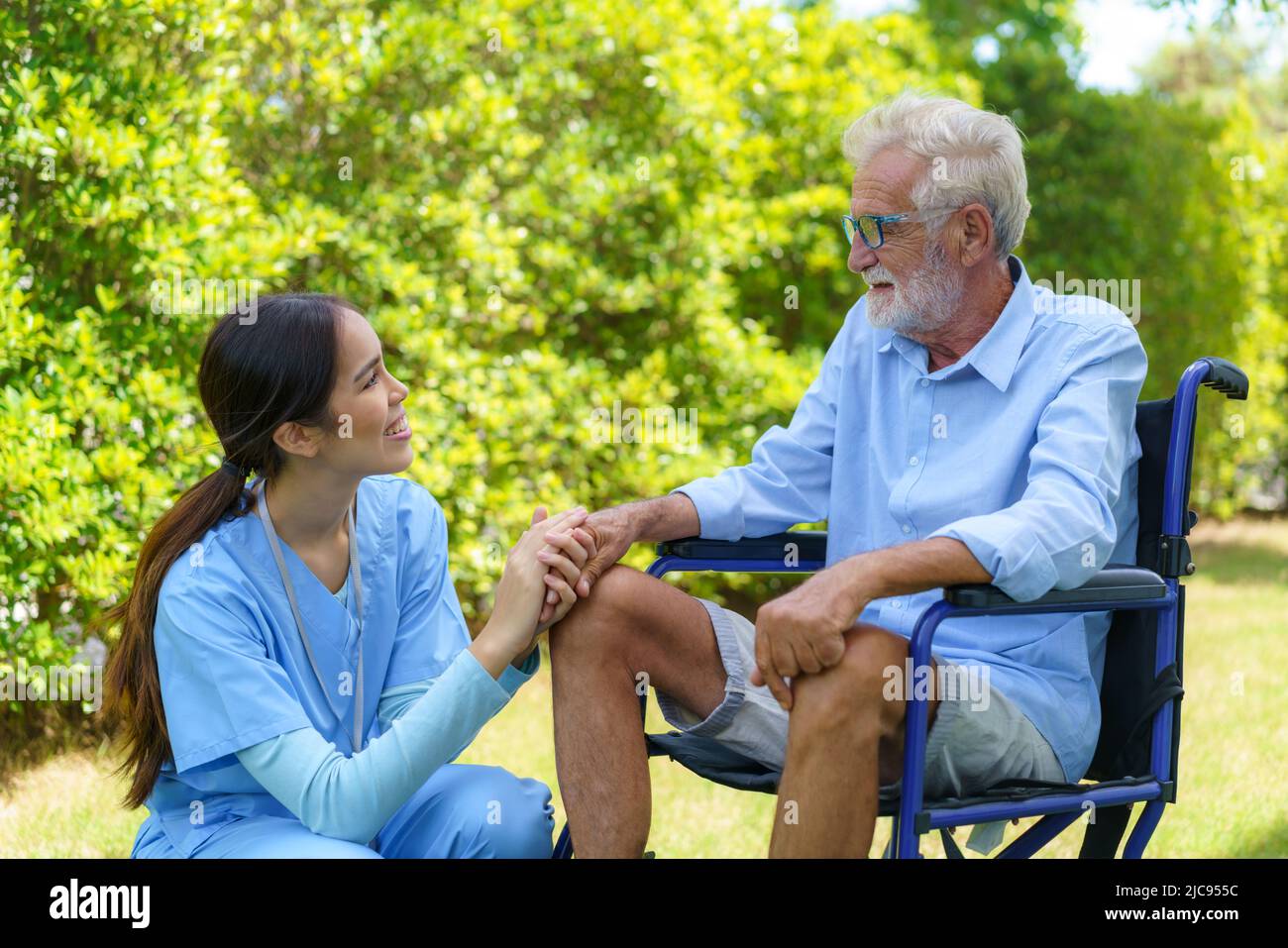 Asian nurse sitting on a hospital bed next to an older man helping hands care in garden at home. Elderly patient care and health lifestyle, medical co Stock Photo