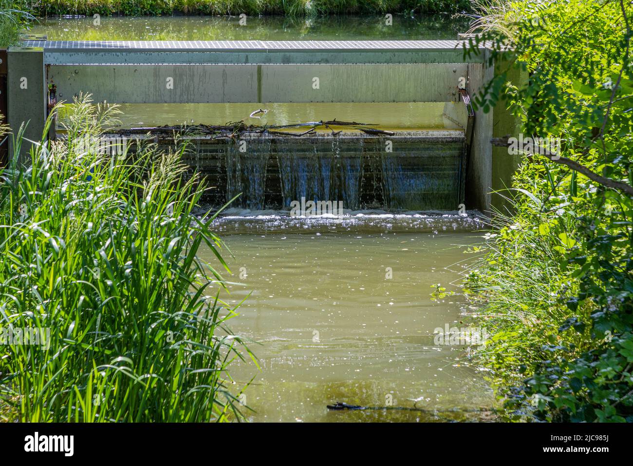 Stream with water flowing into a small weir under a bridge with a metal ...