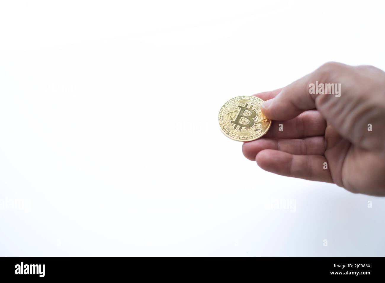 a hand with a bit coin on a white background, selective focus on the coin, cryptocurrency, form of payment, cryptocurrencies accepted, copy space, sel Stock Photo