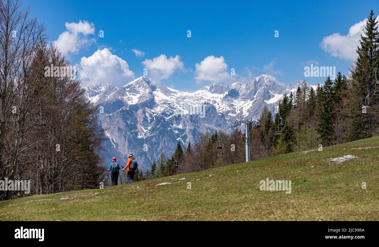 A picture of the landscape of Velika Planina, or Big Pasture Plateau, with the Kamnik–Savinja Alps on the background, and a hiker couple on the bottom Stock Photo