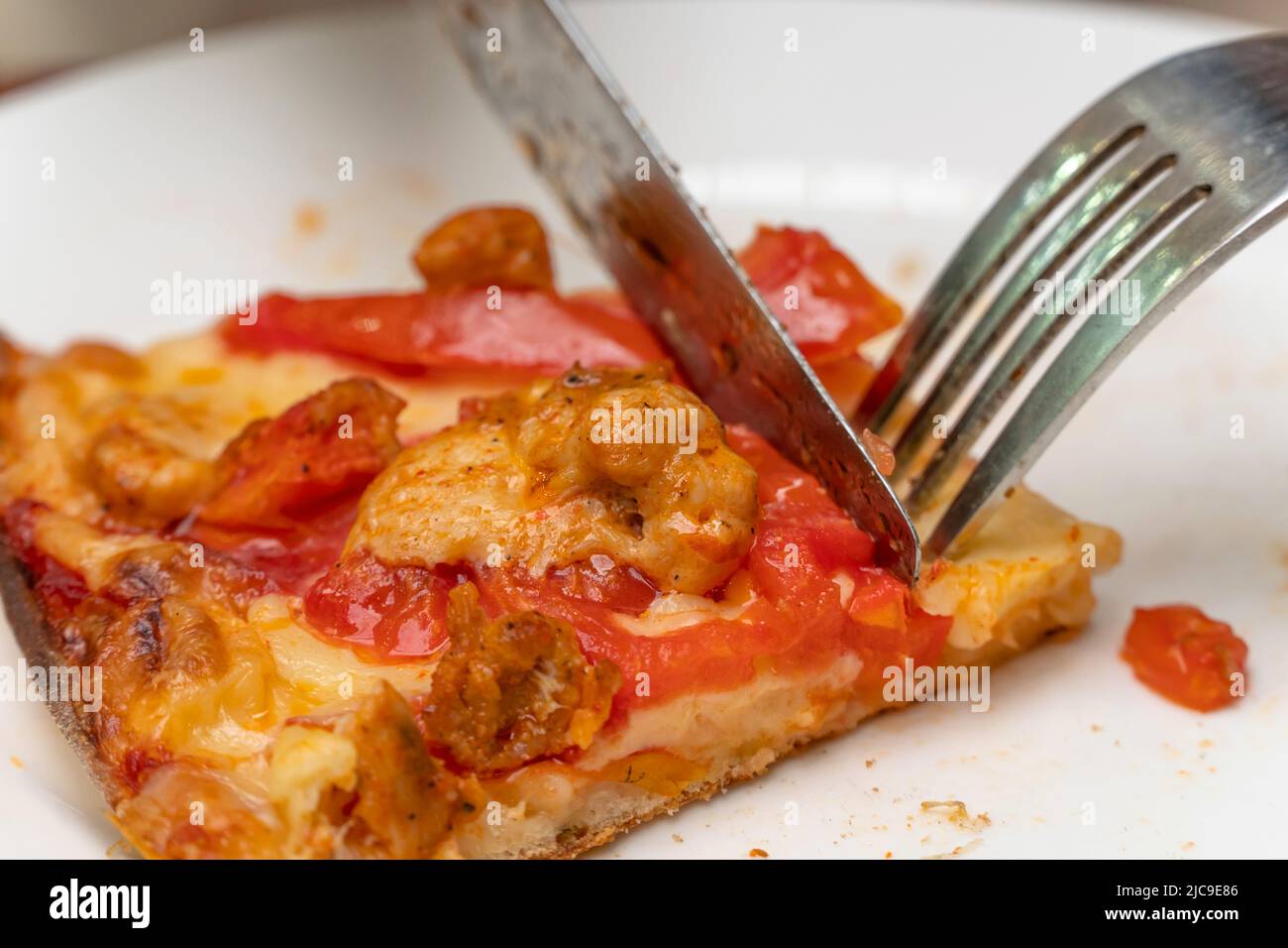 A slice of pizza on a plate close-up. Eat pizza with a knife and fork. Use cutlery at lunch. Juicy slice of pizza. Italian cuisine. Stock Photo