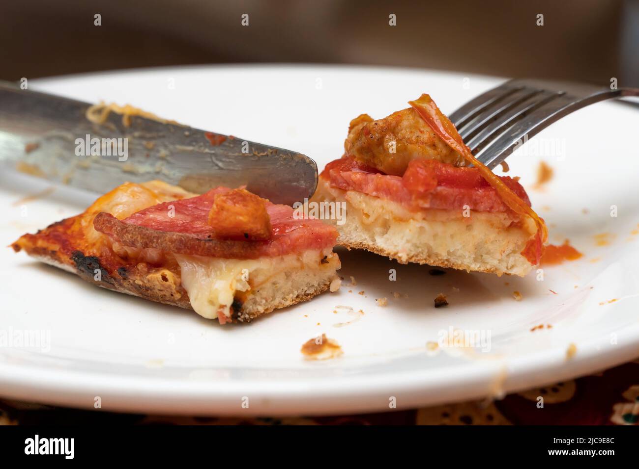 A slice of pizza on a plate close-up. Eat pizza with a knife and fork. Use cutlery at lunch. Juicy slice of pizza. Italian cuisine. Stock Photo