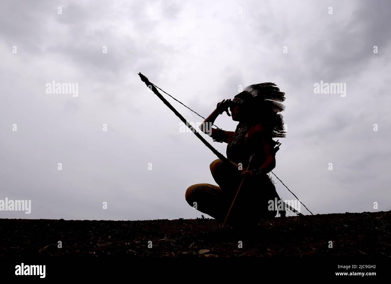 A young native American Indian girl is silhouetted in front of the evening sky. She stands proud with her weapons by her side. Stock Photo