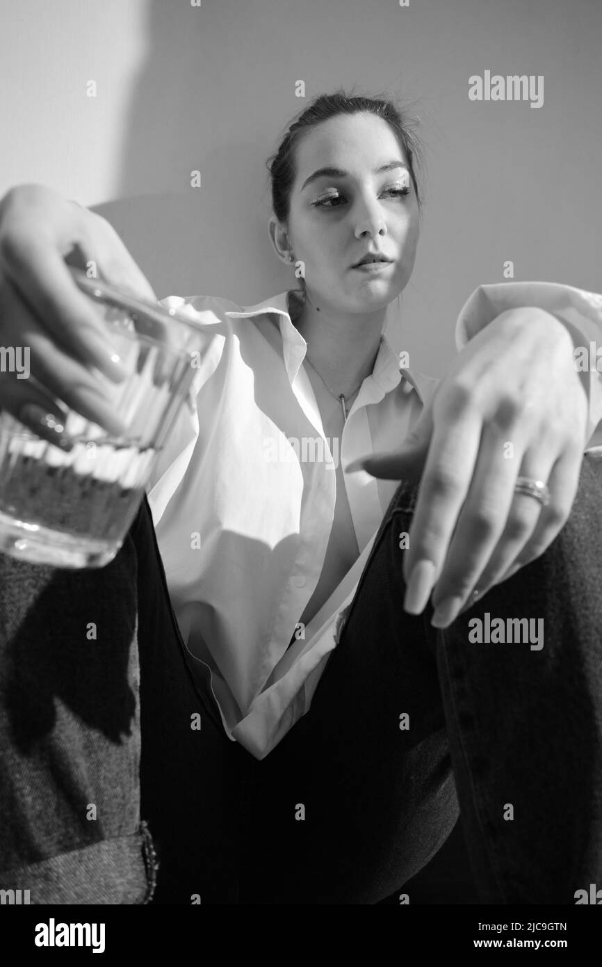 Young woman drinking alcohol from glass against sunny wall background