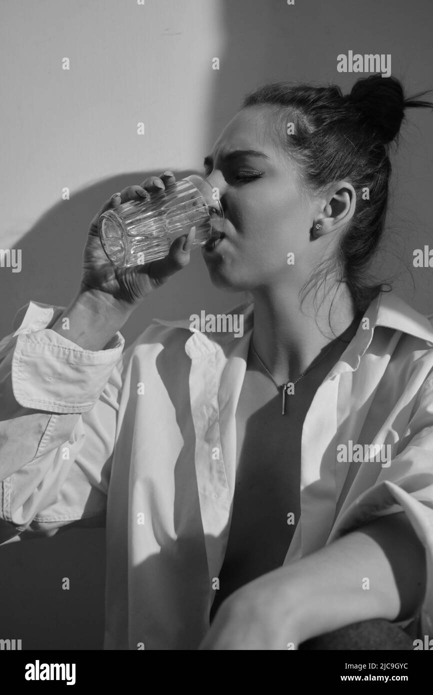 Young woman drinking alcohol from glass against sunny wall background