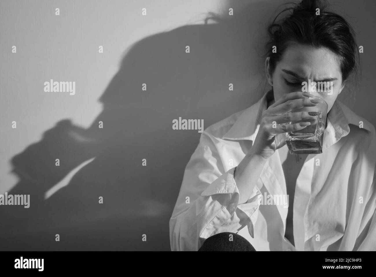 Young woman drinking alcohol from glass against sunny wall background ...