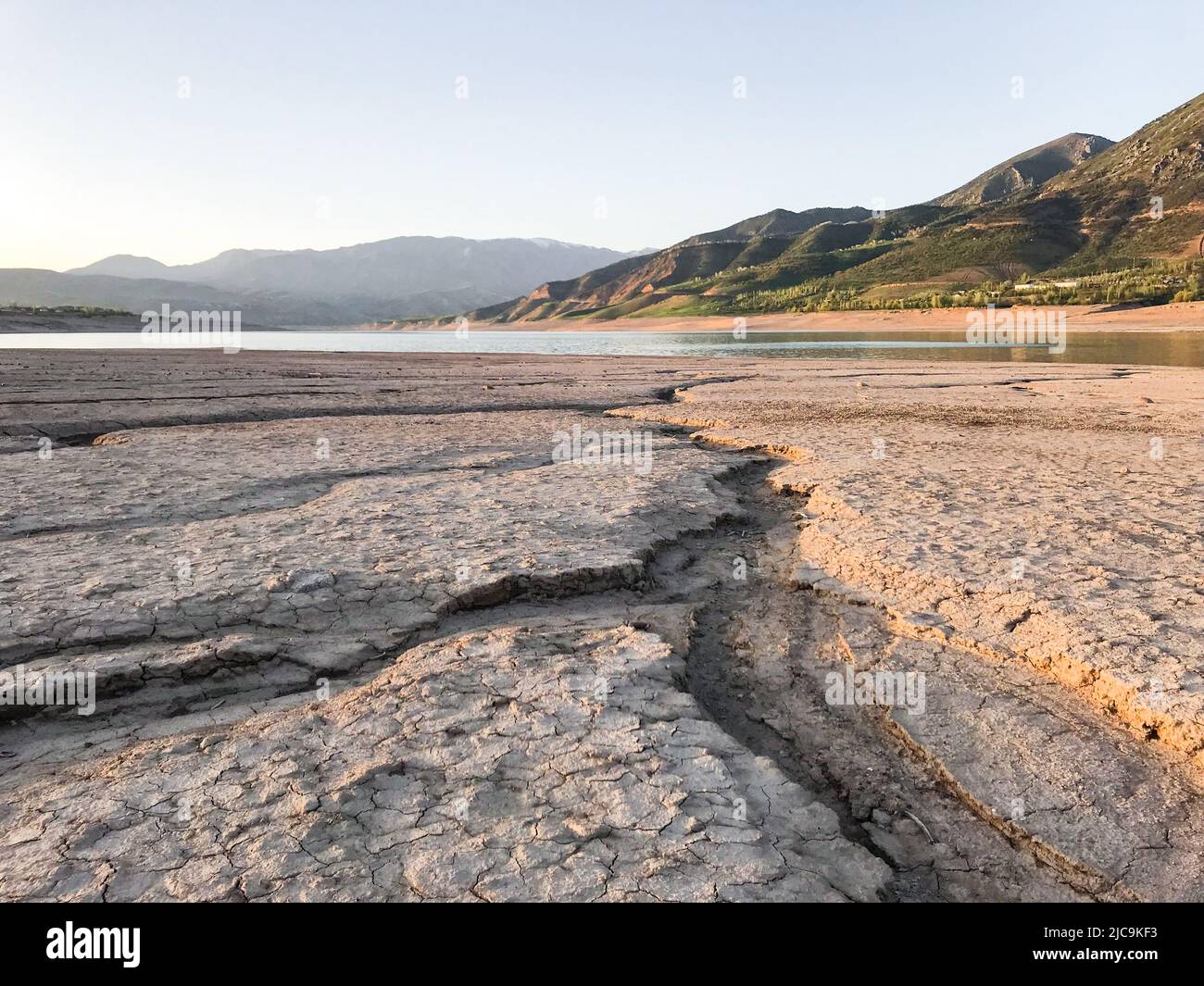 Beautiful landscape with setting sun: mountains, lake, cracked earth with stones -dried-up riverbend. Stock Photo