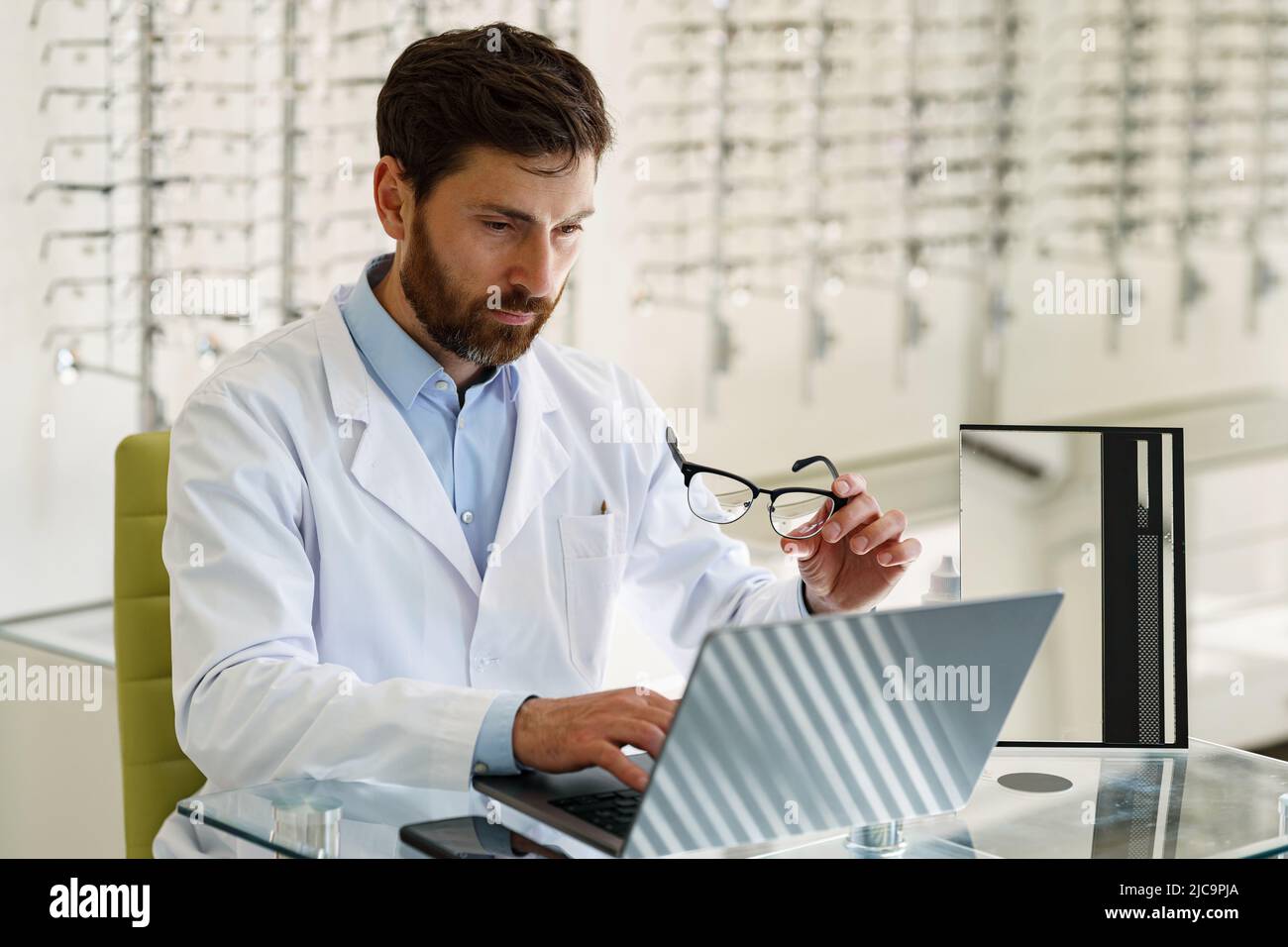 Ophthalmologist working on laptop at his workplace in optic store Stock Photo