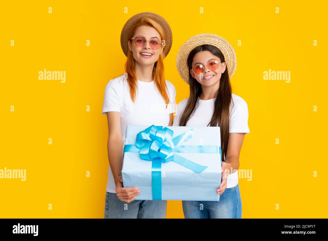 Family of mother and daughter in casual clothes celebrating, hold red present box gift, isolated on yellow background, studio portrait. Stock Photo