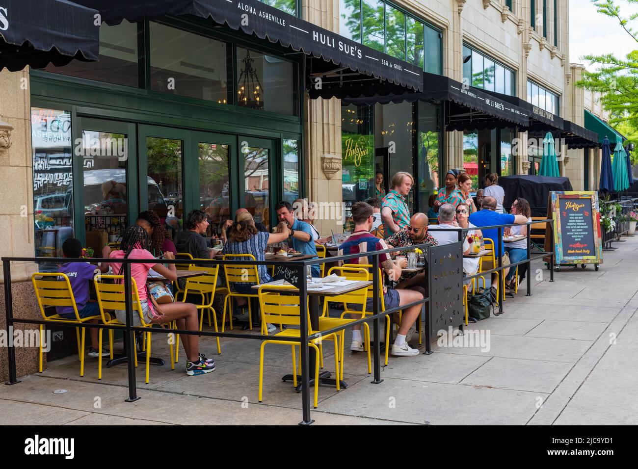 ASHEVILLE, NC, USA-5 JUNE 2022: Huli Sue's BBQ & Grill on Page Ave. in the Grove Arcade busy with sidewalk diners. Stock Photo