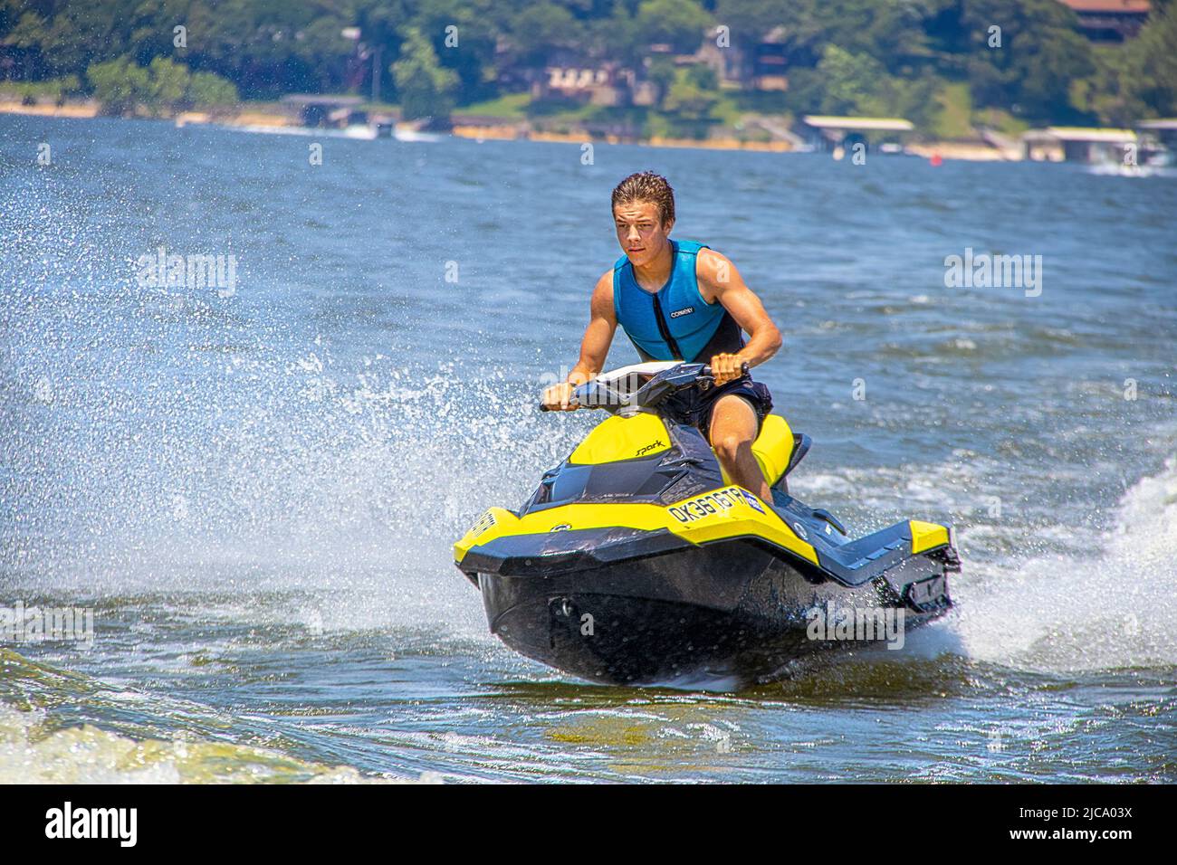 2021 - 06 -20 Grand Lake, OK USA - Attractive young man on wave runner - PWC - jet ski crouched and leaning forward as he prepares  to jump a boats wa Stock Photo