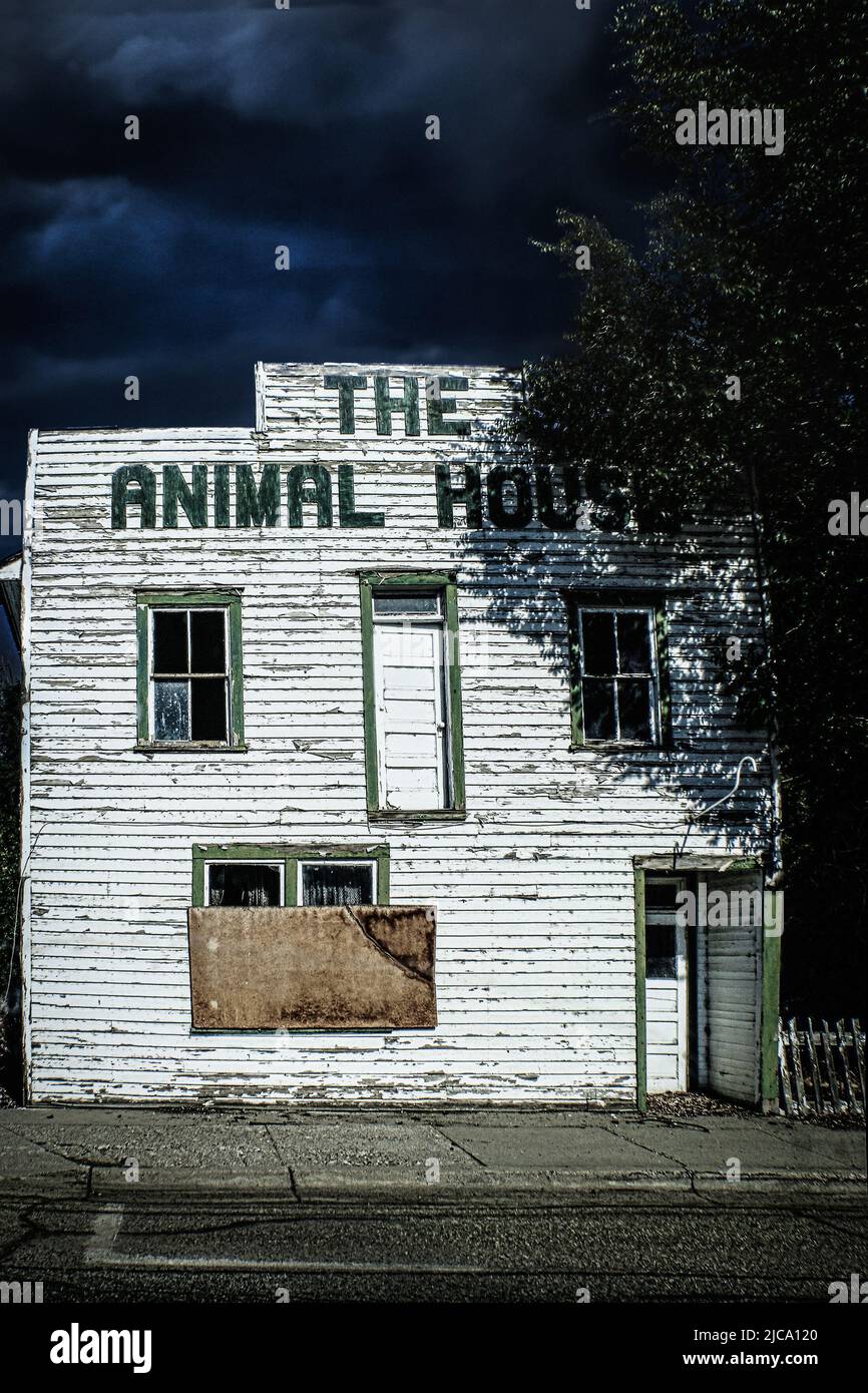 Abandoned Animal Hospital in small town American at dusk with dark sky and windows boarded up and strange second story door leading nowhere Stock Photo