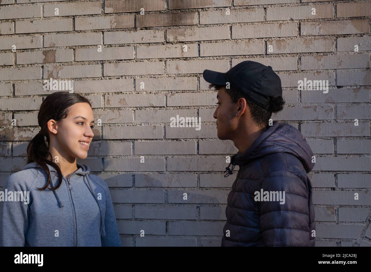 Young couple talking and smiling standing against a brick wall. Love signals between teenagers. Stock Photo