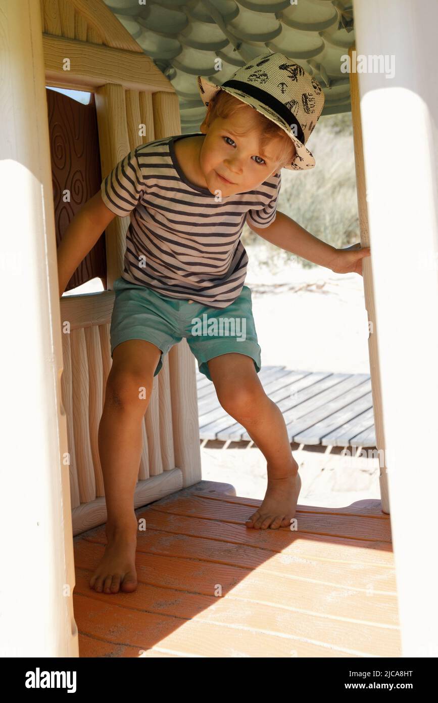 A little boy in a striped shirt in a small plastic playhouse on the beach Stock Photo