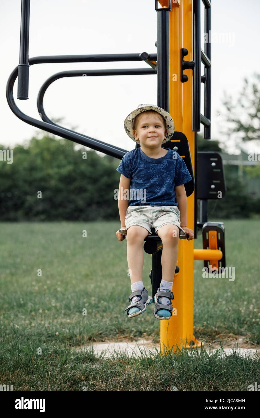 Boy athlete on outdoor sports ground. Child sitting on yellow outdoor exercise machine for teenagers. Stock Photo